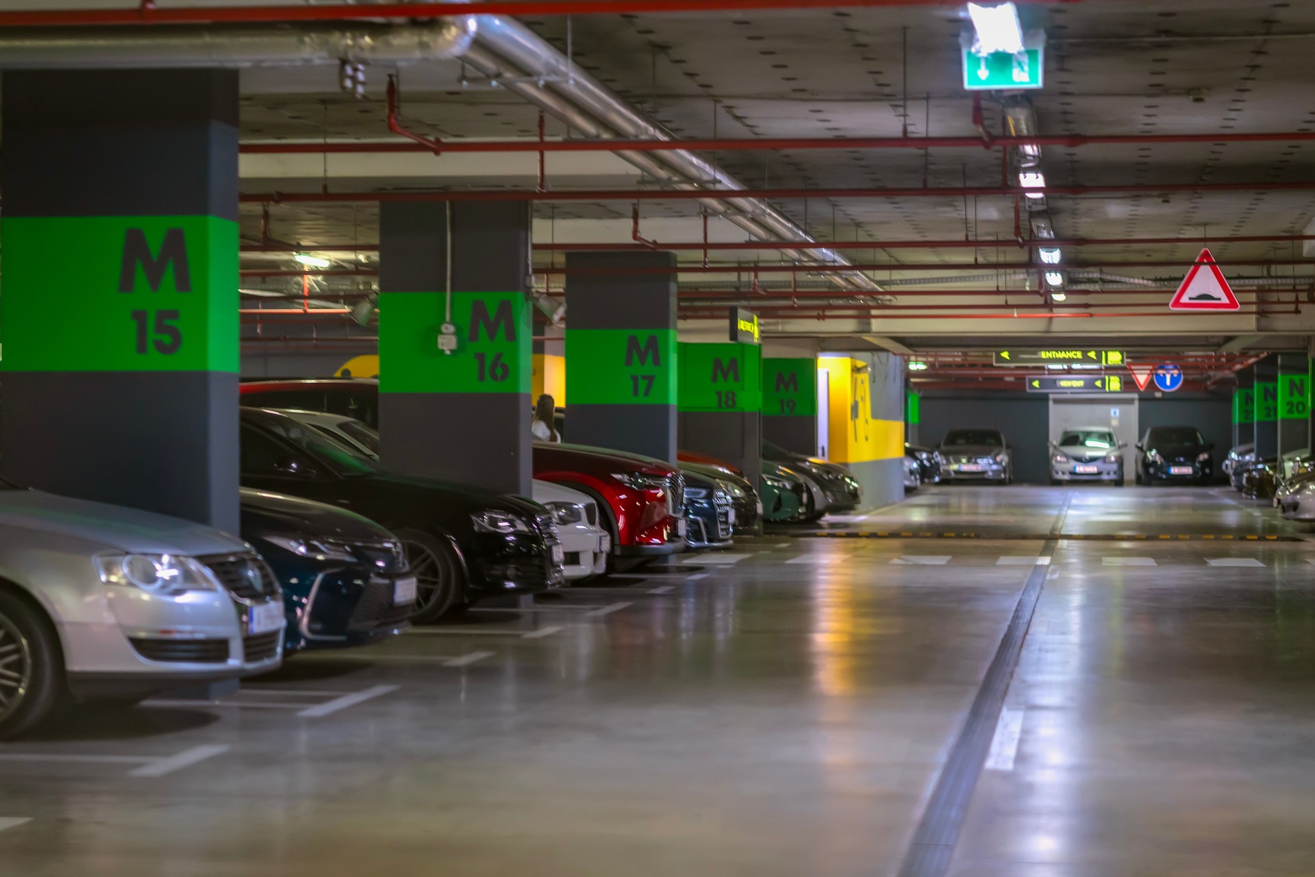 Underground parking lot with green section markings, parked cars, bright lighting in modern city facility, shopping center, mall. Concept of urban parking, vehicle storage, transport infrastructure
